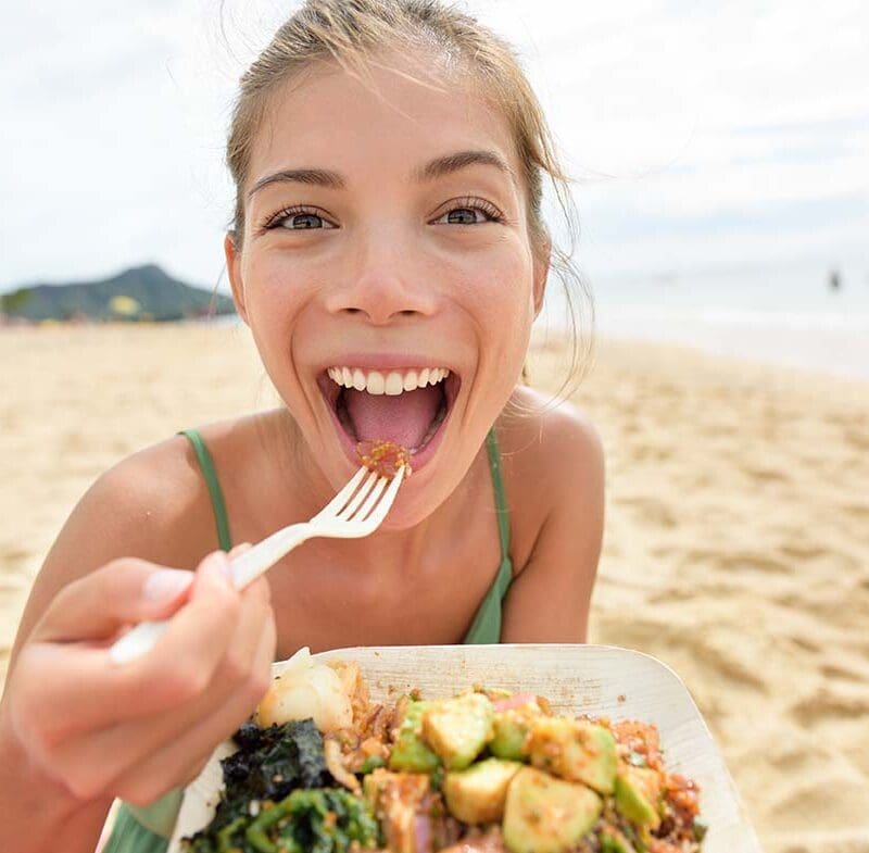 Funny woman eating salad healthy meal on beach