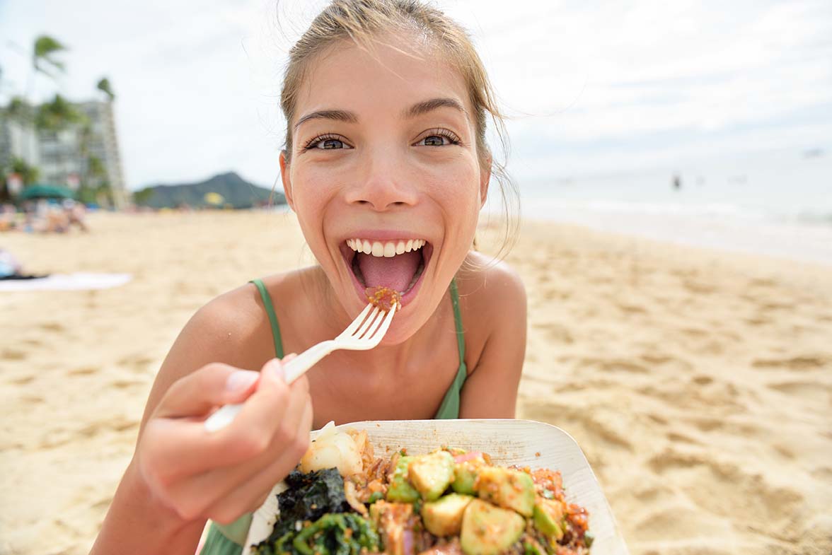 Funny woman eating salad healthy meal on beach
